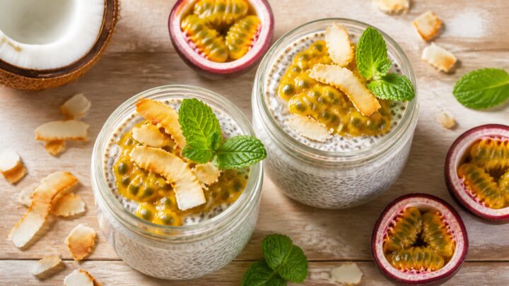Two glass jars of passionfruit coconut chia pudding topped with fresh passionfruit pulp and toasted coconut flakes on a wooden surface