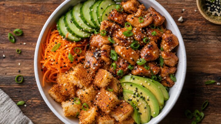 Miso Butter Chicken Crunch Rice Bowl with crispy rice, miso butter chicken, cucumber, carrots, avocado, and green onions on a wooden table