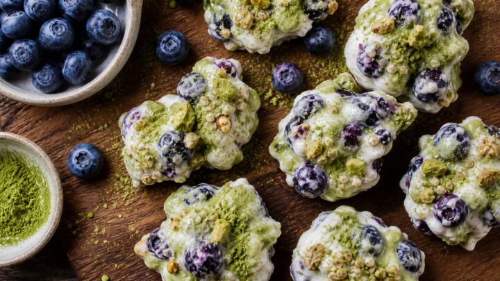 Crunchy blueberry matcha yogurt bark clusters on a white plate with fresh blueberries and matcha powder scattered around