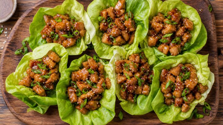 Yuzu honey chicken lettuce cups arranged on a wooden board with fresh butter lettuce leaves and sesame seeds