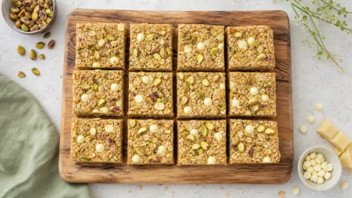 Pistachio white chocolate oat bars cut into squares on a wooden board, showing chewy texture and white chocolate chips.