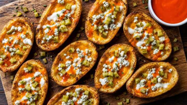 Crispy air fryer buffalo pickle potato skins with melted cheese and ranch drizzle on a white plate.