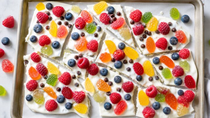 Frozen Greek yogurt gummy bark on a baking sheet, broken into pieces, with colorful gummy fruit candies and berries.