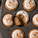 Carrot cake baked oatmeal cups with protein frosting in a muffin tin, topped with frosting and chopped nuts.