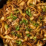 Crispy miso cabbage noodle stir fry in a skillet, topped with green onions and sesame seeds, Asian-inspired vegetarian dinner.