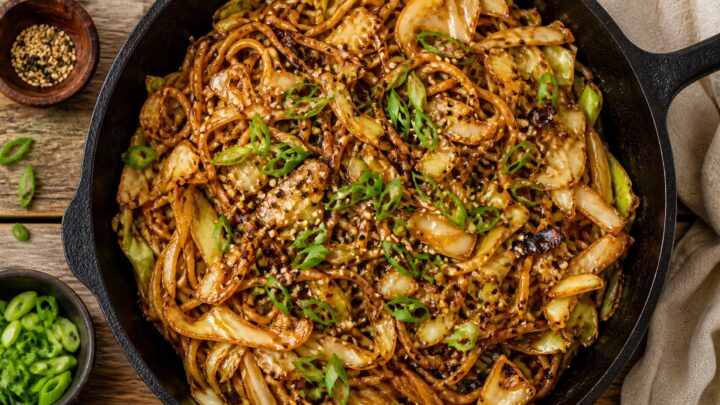 Crispy miso cabbage noodle stir fry in a skillet, topped with green onions and sesame seeds, Asian-inspired vegetarian dinner.