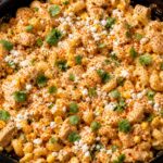 A creamy street corn chicken pasta skillet in a cast iron pan, garnished with cotija cheese, cilantro, and chili powder