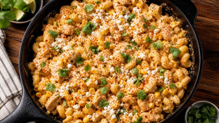 A creamy street corn chicken pasta skillet in a cast iron pan, garnished with cotija cheese, cilantro, and chili powder
