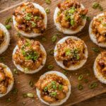 Passionfruit sticky chicken in rice cups garnished with sesame seeds and green onions on a white plate.