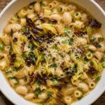 Bowl of brothy butter bean pasta topped with crispy cabbage and Parmesan cheese