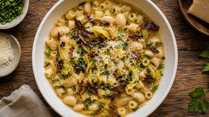 Bowl of brothy butter bean pasta topped with crispy cabbage and Parmesan cheese