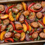 Hot honey peach chicken sausage sheet pan dinner with caramelized peaches and bell peppers on a baking sheet