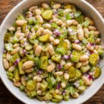 A bowl of crunchy dill pickle white bean salad with fresh dill garnish, served on a wooden table