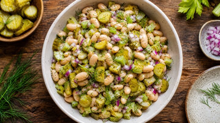 A bowl of crunchy dill pickle white bean salad with fresh dill garnish, served on a wooden table