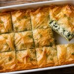 Golden baked cottage cheese spanakopita breakfast casserole in a 9x13 dish with flaky phyllo top and a slice lifted out showing creamy spinach and feta filling