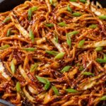 Crispy gochujang cabbage grilled noodles in a skillet with charred cabbage ribbons, green onions, and sesame seeds on top.
