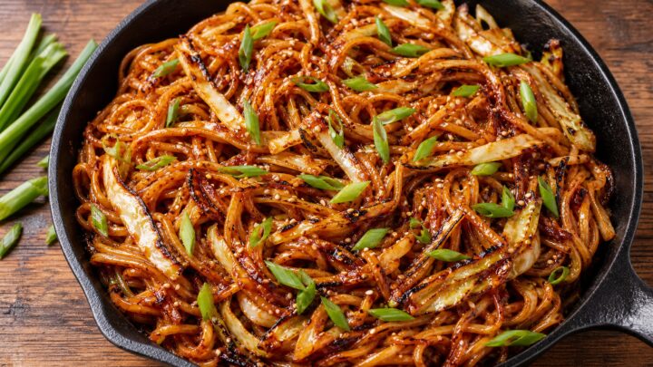 Crispy gochujang cabbage grilled noodles in a skillet with charred cabbage ribbons, green onions, and sesame seeds on top.
