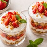 Strawberry miso shortcake cups in small glass dessert dishes, layered with golden crumble, juicy strawberries, and whipped cream, garnished with mint