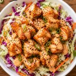 Air fryer bang bang salmon bites over cabbage slaw in a bowl, garnished with green onions and sesame seeds
