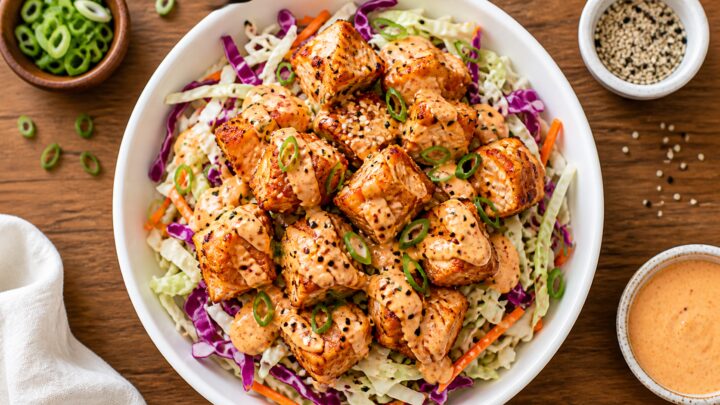 Air fryer bang bang salmon bites over cabbage slaw in a bowl, garnished with green onions and sesame seeds