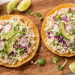 Crispy ranch cabbage and white bean tostadas on a plate with lime wedges and avocado slices
