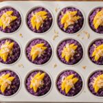 A row of vibrant purple ube coconut sticky rice breakfast cups topped with shredded coconut and fresh mango slices on a rustic wooden board.
