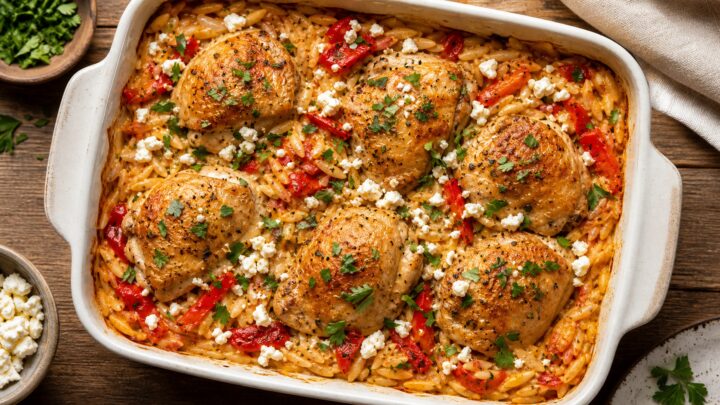 Roasted red pepper feta chicken orzo bake in a white baking dish, garnished with parsley.