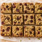 Cherry pistachio baked oat bars cut into squares on a cooling rack, with a cup of coffee nearby.