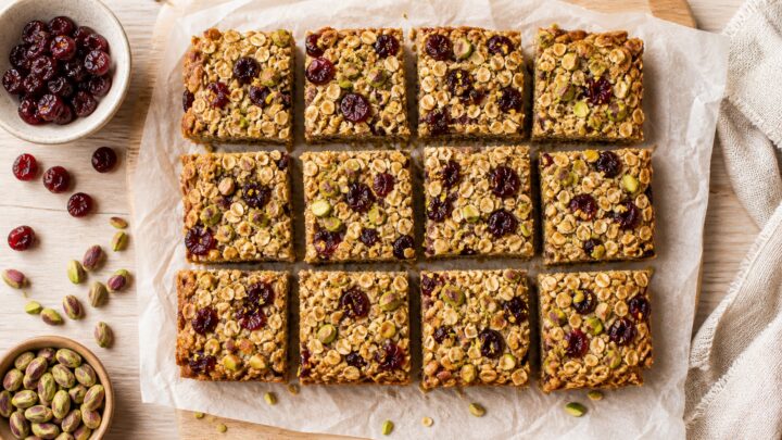 Cherry pistachio baked oat bars cut into squares on a cooling rack, with a cup of coffee nearby.