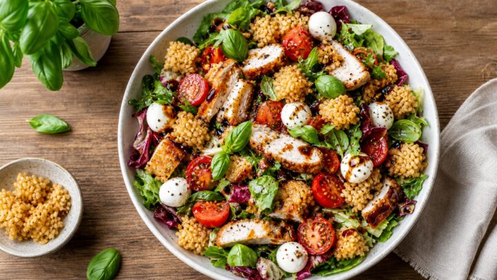 Crispy rice chicken parm salad with greens, cherry tomatoes, fresh mozzarella, and balsamic dressing in a bowl
