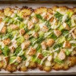 Chicken Caesar Smashed Potato Pizza on a baking sheet with crispy golden crust, melted cheese, and fresh romaine topping.