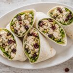 Pistachio cherry chicken salad wrap sliced in half on a plate with pistachios and cherries scattered around