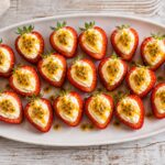 Passionfruit cheesecake stuffed strawberries on a white platter with passionfruit seeds.