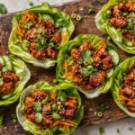 Air Fryer Gochujang Maple Chicken Lettuce Cups with fresh vegetables and sesame seeds on a wooden board