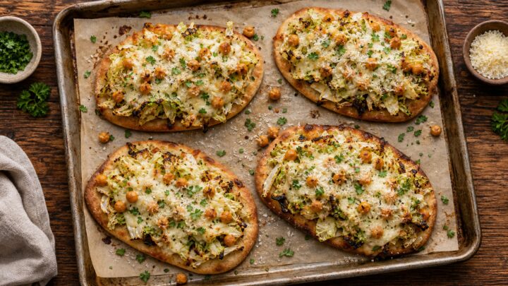 Cabbage Caesar Chickpea Flatbread Melts on a baking sheet, topped with melted cheese and fresh parsley
