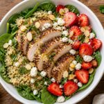 Strawberry Sumac Chicken Grain Bowls with quinoa, spinach, sliced chicken, strawberries, feta, almonds, and lemon vinaigrette in a white bowl.