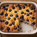Golden blueberry cardamom cottage cheese pancake bake in a baking dish with blueberries scattered on top