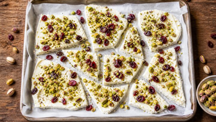 Pistachio labneh breakfast bark on a parchment-lined baking sheet, broken into pieces, with visible pistachios and dried cranberries.