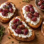 Roasted grape and thyme cottage cheese toasts on a wooden board, with red grapes and fresh thyme garnish.