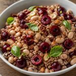 Cherry balsamic farro bowl with white beans, fresh cherries, and basil on a white plate, topped with toasted almonds, perfect for meal prep.