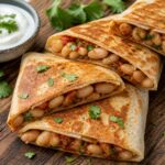 Golden brown harissa butter bean crunch wraps cut in half, served with cilantro and yogurt on a wooden board.
