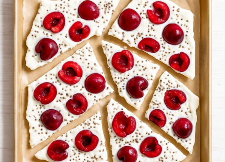 Cherry chia yogurt bark broken into pieces on a baking sheet, showing creamy yogurt with cherries and chia seeds.