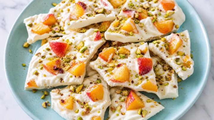Frozen yogurt bark with peaches and pistachios broken into pieces on a white plate