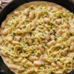 Roasted garlic cabbage alfredo beans in a cast iron skillet topped with fresh parsley