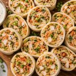 Kimchi Ranch Chicken Salad Pinwheels arranged on a white platter with fresh herbs garnish