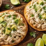 Lemon herb chicken white bean smash tostadas topped with avocado and cotija cheese on a wooden board