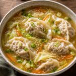 Bowl of miso ginger cabbage turkey dumpling soup with green onions and sesame seeds