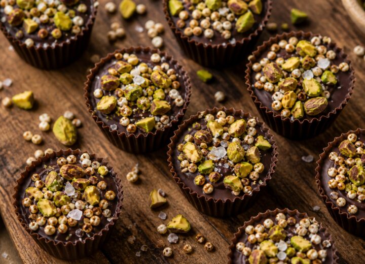 Pistachio dark chocolate quinoa crunch cups arranged on a wooden board, showing the textured top with pistachios and sea salt