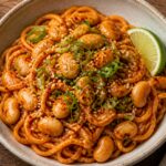 A bowl of gochujang butter bean noodles with green onions and sesame seeds on top