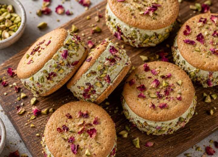 pistachio rose frozen yogurt sandwiches on a plate with pistachios and rose petals